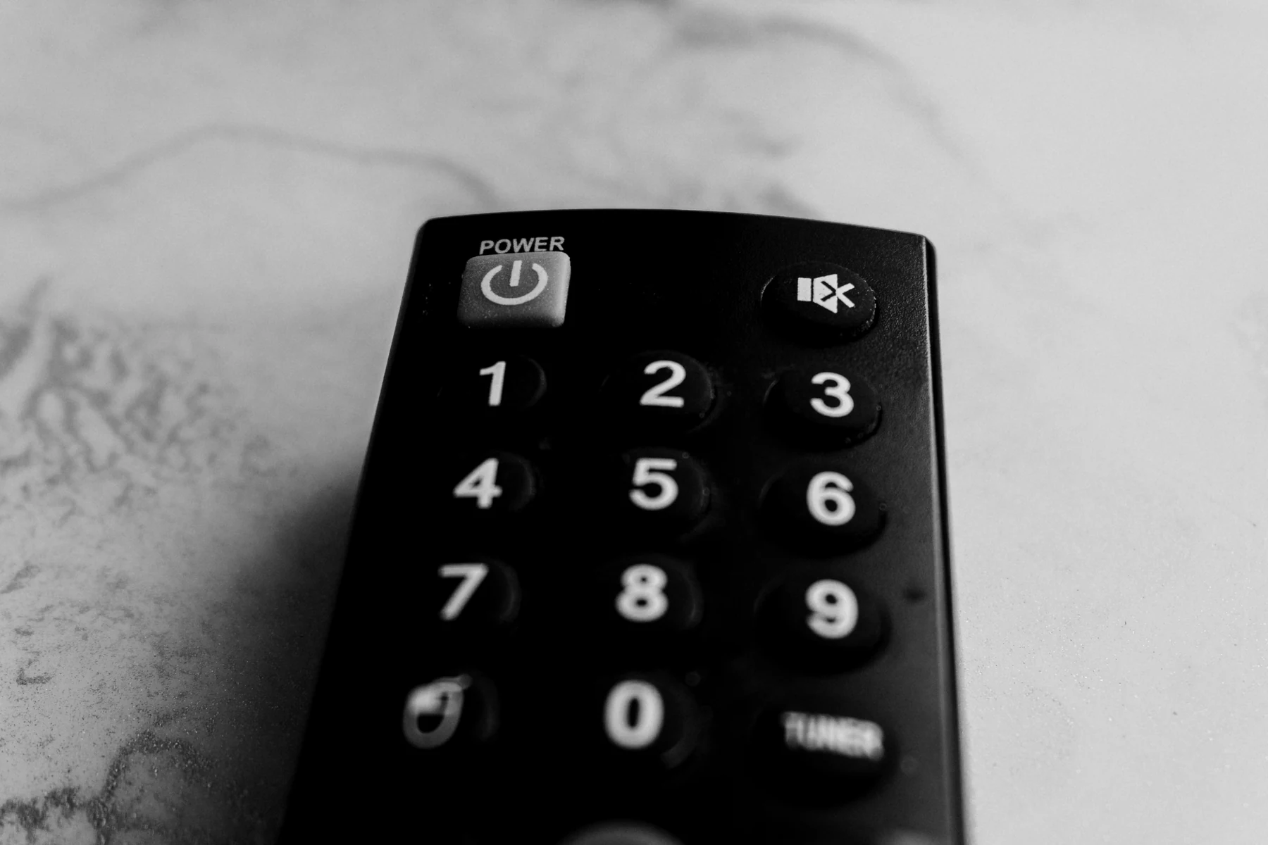 Prim-plan alb-negru al butoanelor numerice și de pornire de pe o telecomandă TV neagră.